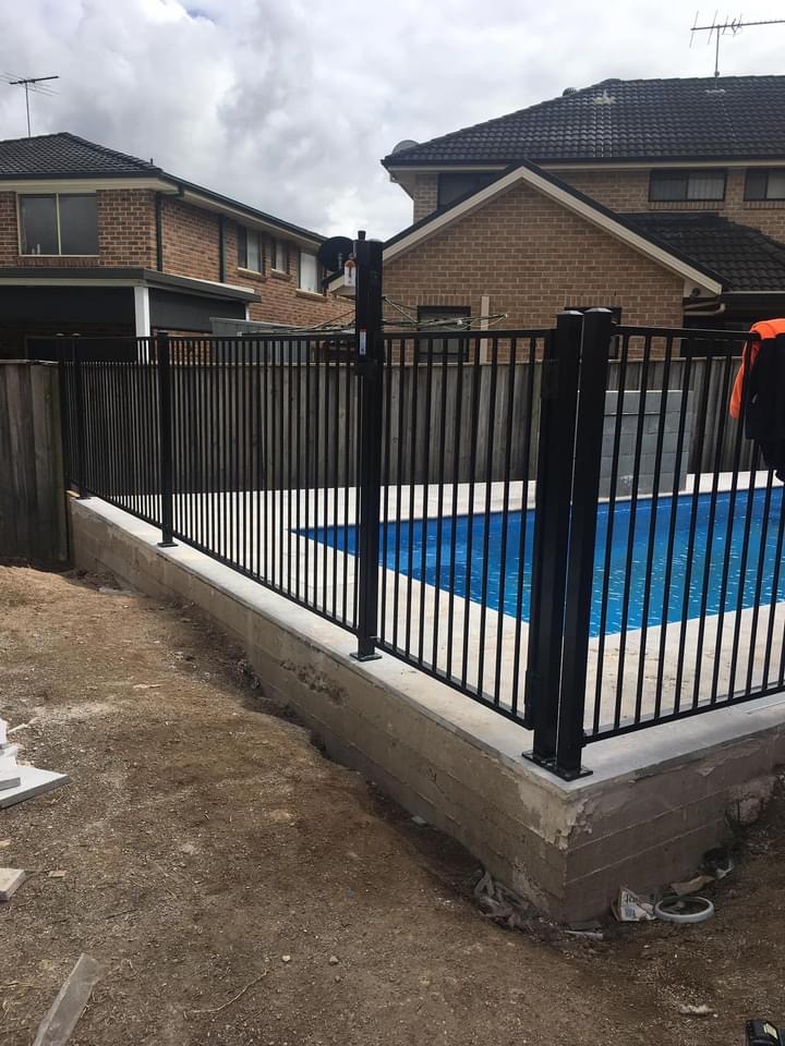 Black aluminium pool safety fencing around an in ground pool