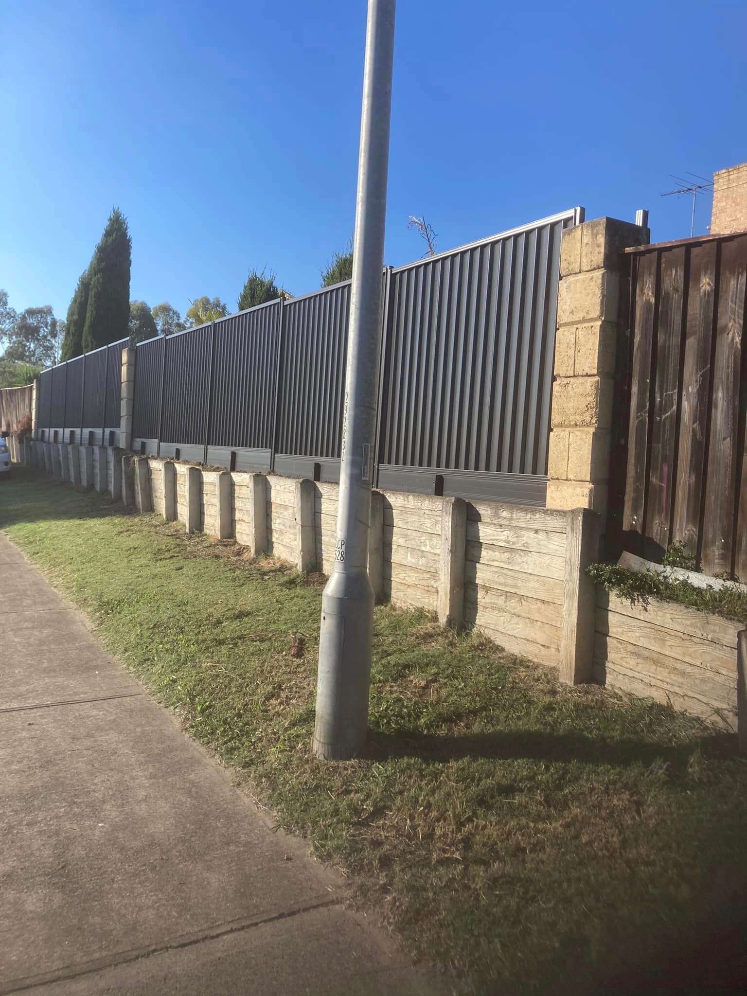 A charcoal Colorbond street boundary above a sleeper retaining wall