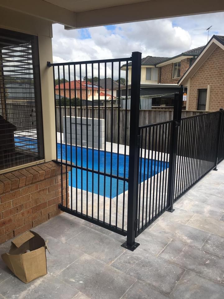 A black aluminium pool gate seen from a paved patio